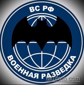 Фото тату в виде круглой эмблемы с изображением летучей мыши и глобуса. Эмблема выполнена в синих и черных тонах с надписями на русском языке.