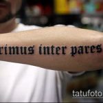 Фото татуировки на руке с латинской надписью 'Primus inter pares'. Черно-белое изображение, готический шрифт.