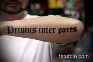 Фото татуировки на руке с латинской надписью 'Primus inter pares'. Черно-белое изображение, готический шрифт.