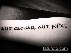 Фото минималистичной татуировки на предплечье с латинской надписью 'aut Caesar, aut Nihil'. Черно-белое изображение, четкие линии.