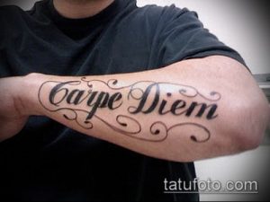 Фото татуировки на предплечье с надписью 'Carpe Diem' и декоративными узорами. Классический и вдохновляющий дизайн.