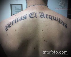 Фото татуировки на спине с латинской надписью 'Veritas Et Aequitas', выполненной в классическом стиле. Строгий и элегантный дизайн.