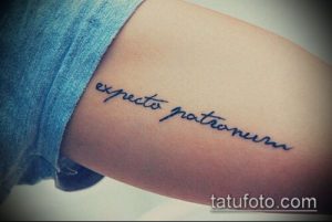 Фото тату с надписью 'Expecto Patronum' на внутренней стороне предплечья, выполненной черными чернилами. Изящный шрифт и минималистичный дизайн.