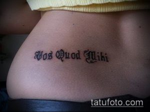 Фото тату на пояснице с латинской надписью 'Vos Quod Miki' в готическом стиле. Элегантный и загадочный дизайн.