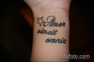 Фото тату на запястье с надписью 'Amor vincit omnia' и маленькой звездочкой. Изящный и лаконичный рисунок для тех, кто ценит простоту.