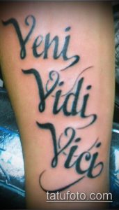 Фото тату с латинской фразой 'Veni Vidi Vici' на предплечье, выполненной черными чернилами в каллиграфическом стиле. Идеально для любителей истории и латыни.