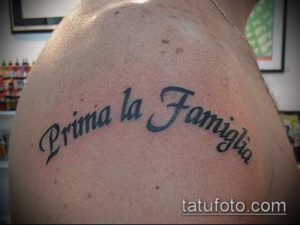 Фото тату надписи 'Prima la Famiglia' на плече. Черный цвет, каллиграфический шрифт, итальянская надпись. Идеи для тату надписей.