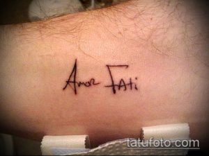Фото минималистичной татуировки надписи 'Amor Fati' на руке, выполненной тонкой линией. Лаконичный и стильный дизайн.