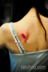 Фото тату маленького красного пера на женской спине. Изящный рисунок татуировки выполнен в минималистичном стиле с акцентом на детали пера.