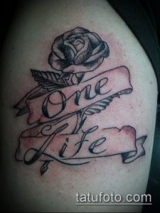 Фото тату розы с надписью 'One Life' на ленте. Черно-серый рисунок татуировки на плече.