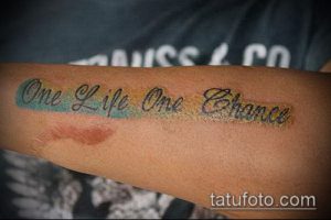 Фото тату на предплечье с надписью 'One Life One Chance', выполненной в ярких цветах: бирюзовом, желтом и оранжевом. Стильный рисунок татуировки.