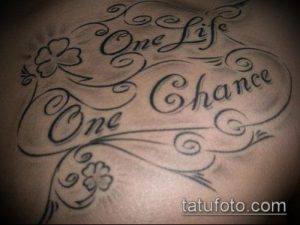 Фото тату надписи 'One Life One Chance' с изображением клевера на груди. Черно-белая татуировка, выполненная в декоративном стиле.