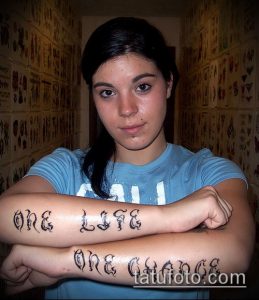 Фото тату надписи 'One Life One Chance' на предплечьях девушки, выполненной готическим шрифтом с эффектом тени. Длинная надпись, занимающая большую часть предплечья.