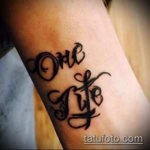 Фото минималистичной татуировки надписи 'One Life' на руке. Черно-серая татуировка с изящными завитушками.