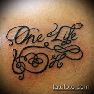 Фото тату надписи 'One Life' с изображением скрипичного ключа и кельтского узла. Черно-серая татуировка на плече.