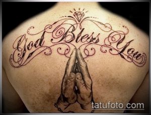 Фото тату на спине: надпись 'God Bless You' и молящиеся руки. Красные акценты и детализированный рисунок татуировки.