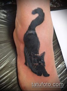 Фото тату черного кота на лодыжке. Реалистичный рисунок с детально проработанной шерстью и выразительными голубыми глазами.