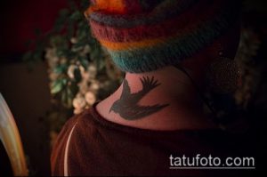 Фото минималистичной татуировки ворона на шее девушки. Черный силуэт птицы в полете, выполненный в простом и элегантном стиле.