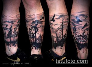 Фотографии татуировок на голенях, изображающих мрачный лес с деревьями и летящими птицами. Использована черно-серая палитра с эффектом брызг краски.