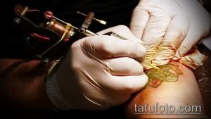 Фото процесса нанесения татуировки цветка на кожу. Мастер работает тату-машинкой, используя перчатки.
