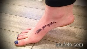 Фото тату надписи "Widen your eyelids" на стопе. Черная надпись, выполненная каллиграфическим шрифтом.