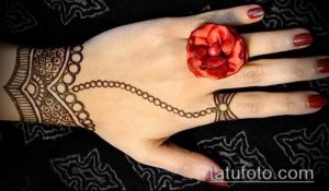 Фото тату хной: сложный узор, покрывающий руку от запястья до пальцев, с использованием коричневой хны и красного цветка в качестве акцента.