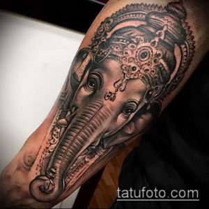 Фото тату портрета Ганеши на руке, выполненное в черно-серых тонах с высокой детализацией. Акцент на выразительных глазах и сложной отделке.