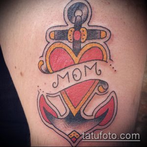 Фото тату на руке: сердце с якорем и надписью 'Mom'. Стиль олд скул, яркие цвета, татуировка для мамы.