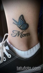 Фото тату на запястье: голубая бабочка с надписью 'Mom', выполненное в изящном и минималистичном стиле.