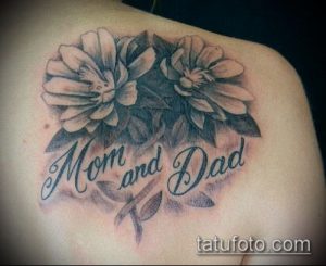 Фото тату: Изображение двух белых цветов с надписью 'Mom and Dad' на плече, выполненное в черно-серых тонах.