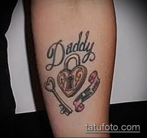Фото тату: Надпись 'Daddy' с изображением сердца в замке и ключом на предплечье, выполненная в ярких цветах.