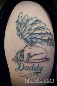 Фото тату на плече с изображением ангела и надписи 'Daddy'. Черно-белая татуировка с детальной прорисовкой крыльев и лица.