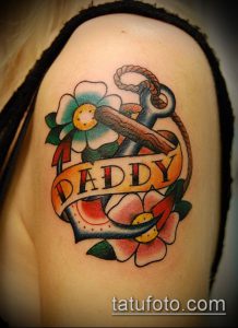 Фото тату на плече в стиле олдскул с изображением якоря, цветов и надписи 'Daddy'. Яркие цвета, четкие контуры, классический дизайн.