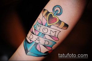 Фото тату якоря с сердцем и надписями 'Mom' и 'Dad' на руке. Память о родителях, морская татуировка в стиле олдскул.