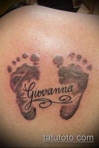 Фото тату на спине с изображением отпечатков детских ножек и надписью "Giovanna". Черно-серый рисунок татуировки.