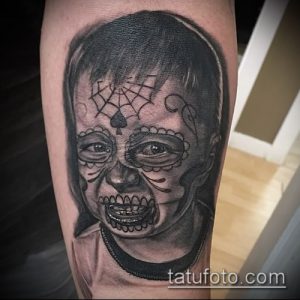 Фото тату: портрет девочки, стилизованный под сахарный череп (calavera), с детальной проработкой и узорами на лице, выполненный в черно-серых тонах на предплечье.