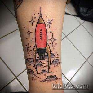 Фото ретро татуировки ракеты на фоне лунного пейзажа. Старый стиль, яркие цвета, космическая тематика.