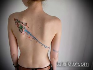 Фото акварельной татуировки на спине с изображением ракеты, оставляющей за собой цветной след, выполненной в нежных пастельных тонах.