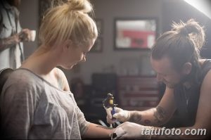 Фото процесса нанесения татуировки на руку девушки: мастер концентрированно работает, а клиентка смотрит в сторону.