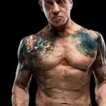 Фотография Сильвестра Сталлоне с масштабными татуировками на руках и груди, демонстрирующими сложную композицию и яркие цвета.