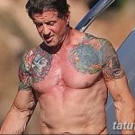 Фотография Слая Сталлоне с многочисленными татуировками на руках и плечах на фоне голубого неба. Видны рисунки черепов и других символов.