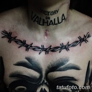 Фото тату на груди: колючая проволока, обвивающая череп, с надписью "VICTORY OR VALHALLA". Детализированный рисунок татуировки в черных тонах.