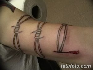 Фото тату колючей проволоки с надписью на руке. Рисунок татуировки выполнен в минималистичном стиле, с использованием тонких линий и четких контуров.