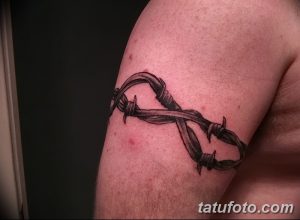 Фото татуировки на плече в виде колючей проволоки. Черно-серый рисунок с реалистичной прорисовкой колючек и текстуры проволоки.