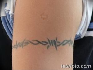 Фото тату колючей проволоки на руке, выполненное в черно-серых тонах. Рисунок имеет стилизованный вид, с акцентом на геометрические формы.