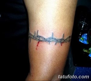 Фото минималистичного тату колючей проволоки с каплями крови на предплечье. Рисунок выполнен в черно-серых тонах, с акцентом на четкость линий.