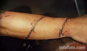 Фото татуировки в виде колючей проволоки на руке: тонкий черный рисунок, обвивающий предплечье.