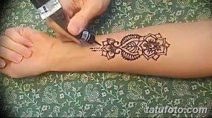 Фото процесса нанесения тату мехенди на руку, демонстрирующее работу мастера с аппликатором. На фоне виден узор, который постепенно проявляется на коже.