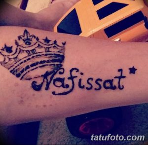 Фото тату хной на руке с изображением короны и надписью 'Nafissat'. Детализированный рисунок, выполненный в черном цвете с добавлением звезд.