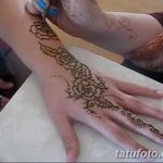 Фото процесса нанесения тату мехенди на руку. Мастер аккуратно наносит хну с помощью специального инструмента, создавая сложный цветочный узор.